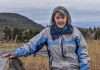 Une femme se tient debout à côté d'une pile de billots de bois