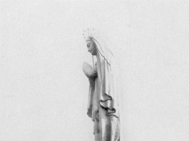 Un homme tout petit se tient au pied de la Statue Notre-Dame-du-Saguenay.
